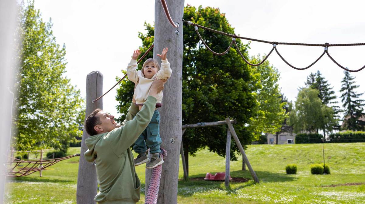 Vater hilft seinem ca. 4-jährigen Kind an ein Klettergerüst.