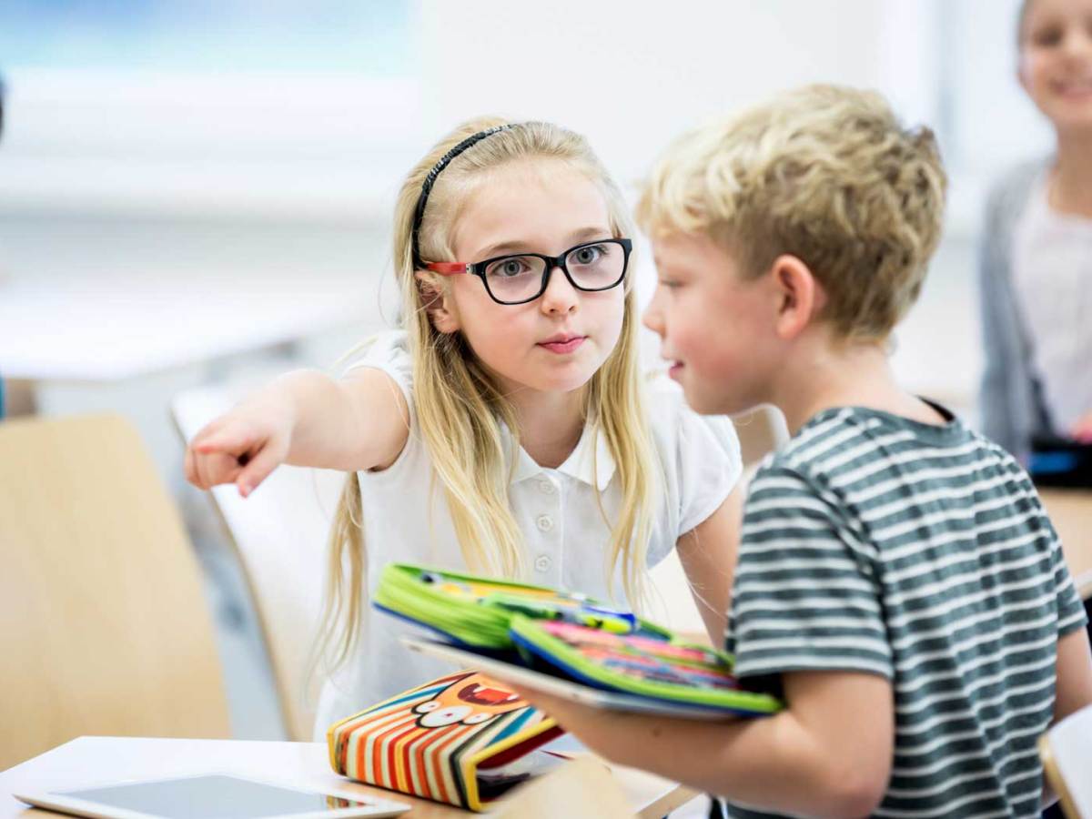 Ein M&auml;dchen zeigt ihrem Mitsch&uuml;ler, wohin er sich setzen soll.