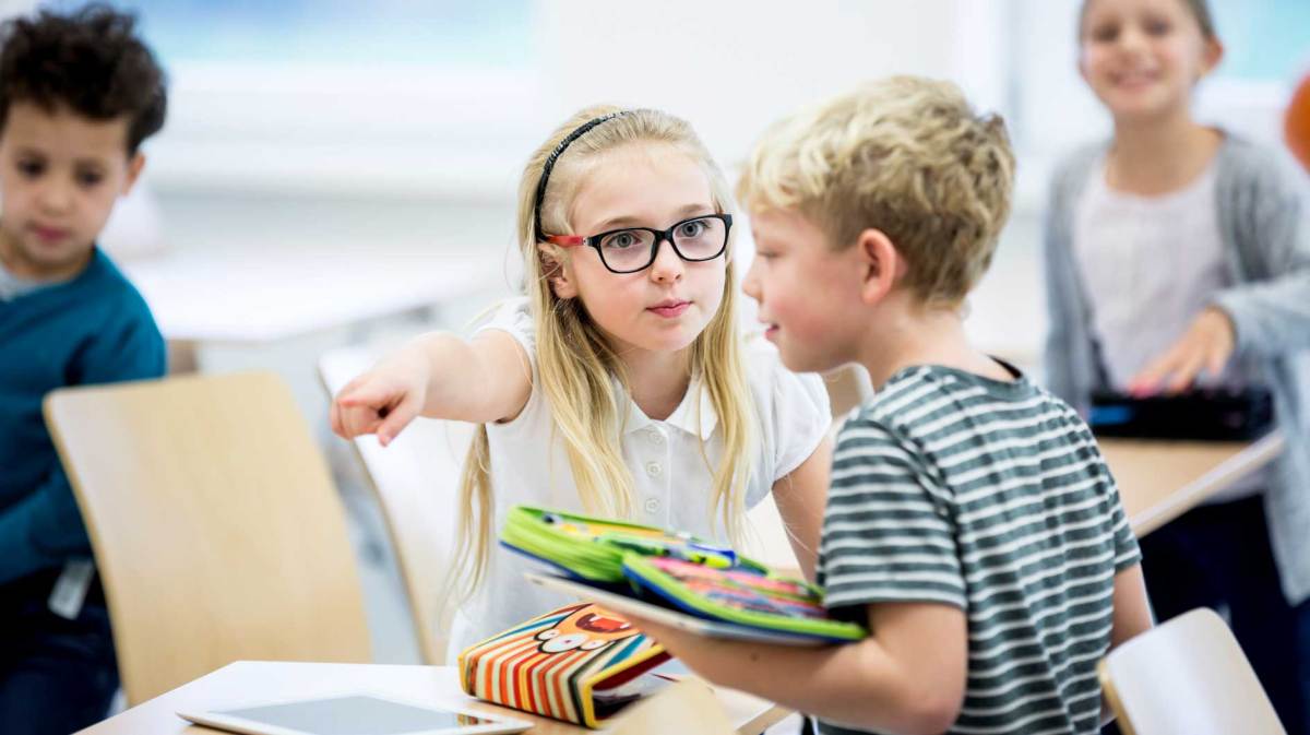 Ein Mädchen zeigt ihrem Mitschüler, wohin er sich setzen soll.