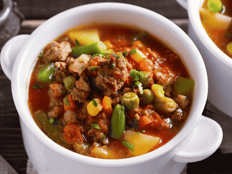 Suppe mit Hackfleisch, Gemüse und Kartoffeln in kleiner, weißer Schüssel.