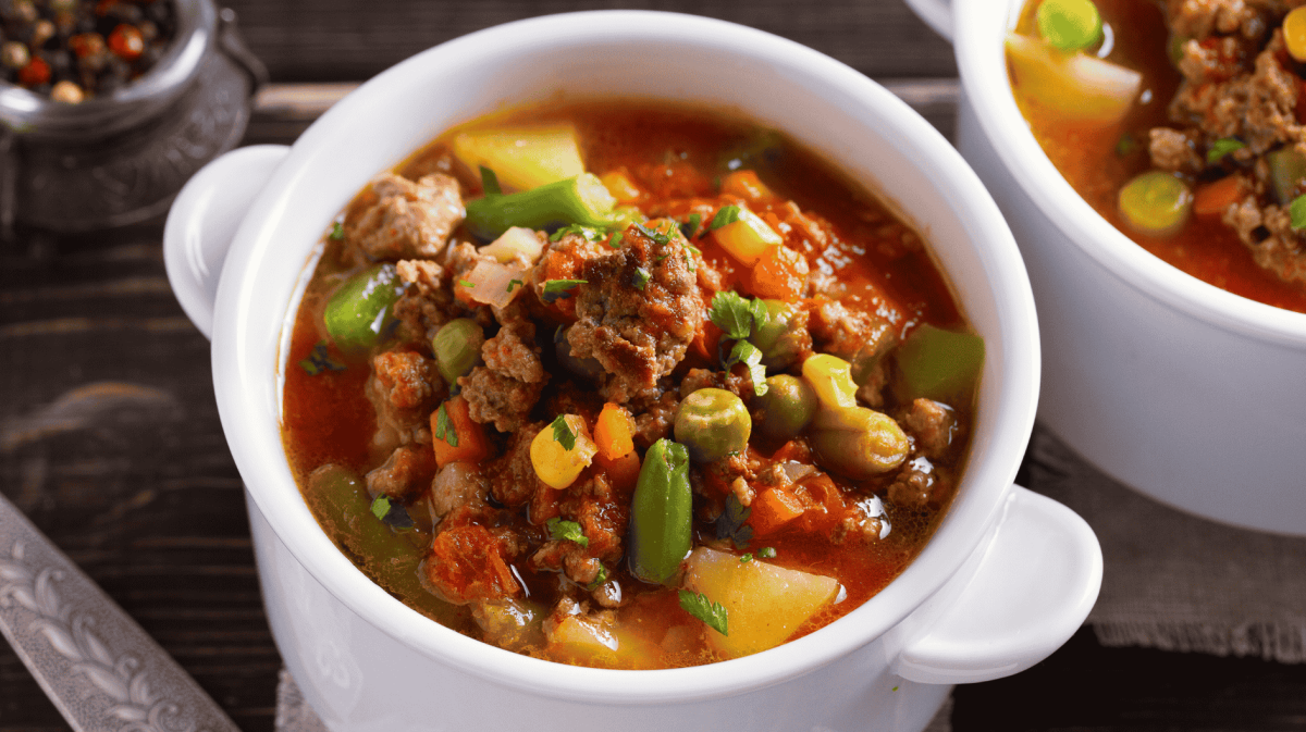 Suppe mit Hackfleisch, Gemüse und Kartoffeln in kleiner, weißer Schüssel.
