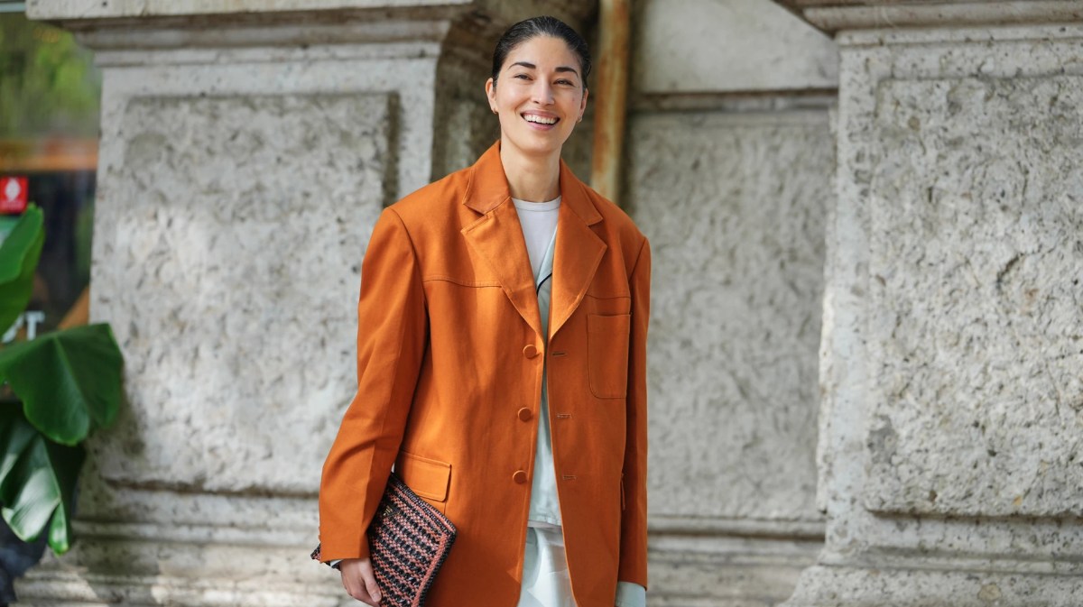 Model trägt einen orangefarbenen Blazer und hat ihre Haare zu einem Dutt gestylt.