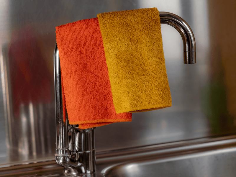 Gelber und Orangener Lappen trocknen auf dem Wasserhahn der Küchenspüle.