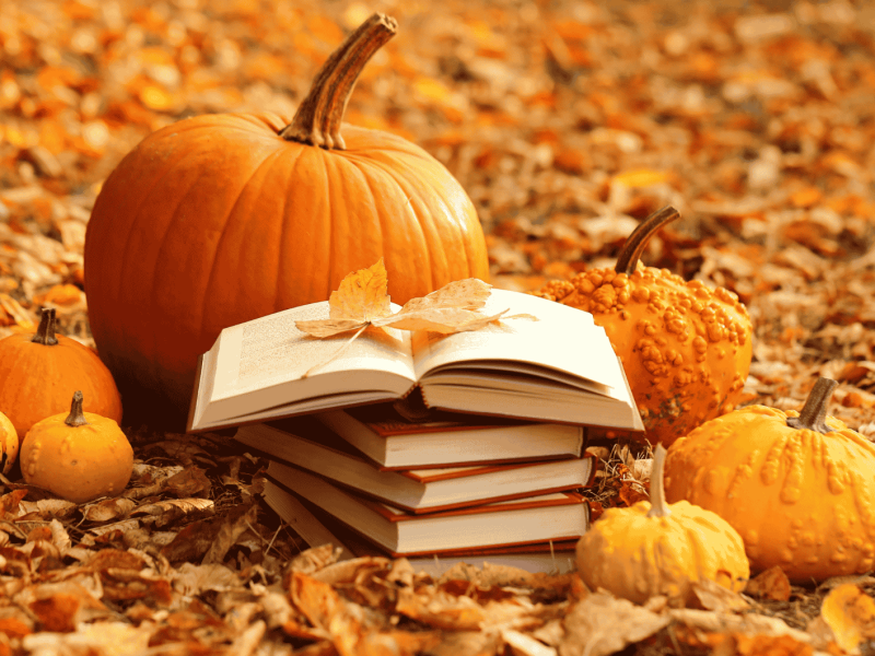 Bücherstapel und Kürbisse in Herbstlaub.