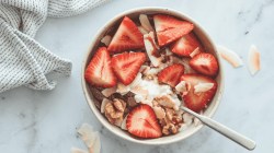 Quark mit Erdbeeren, Getreideflocken, Kokosnuss, Nüssen und Sirup, Marmorhintergrund.