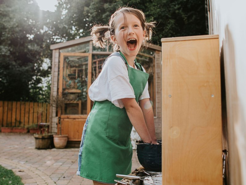 Aufgeregtes Mädchen spielt draußen in einer Matsch-Küche und stiftet Chaos.