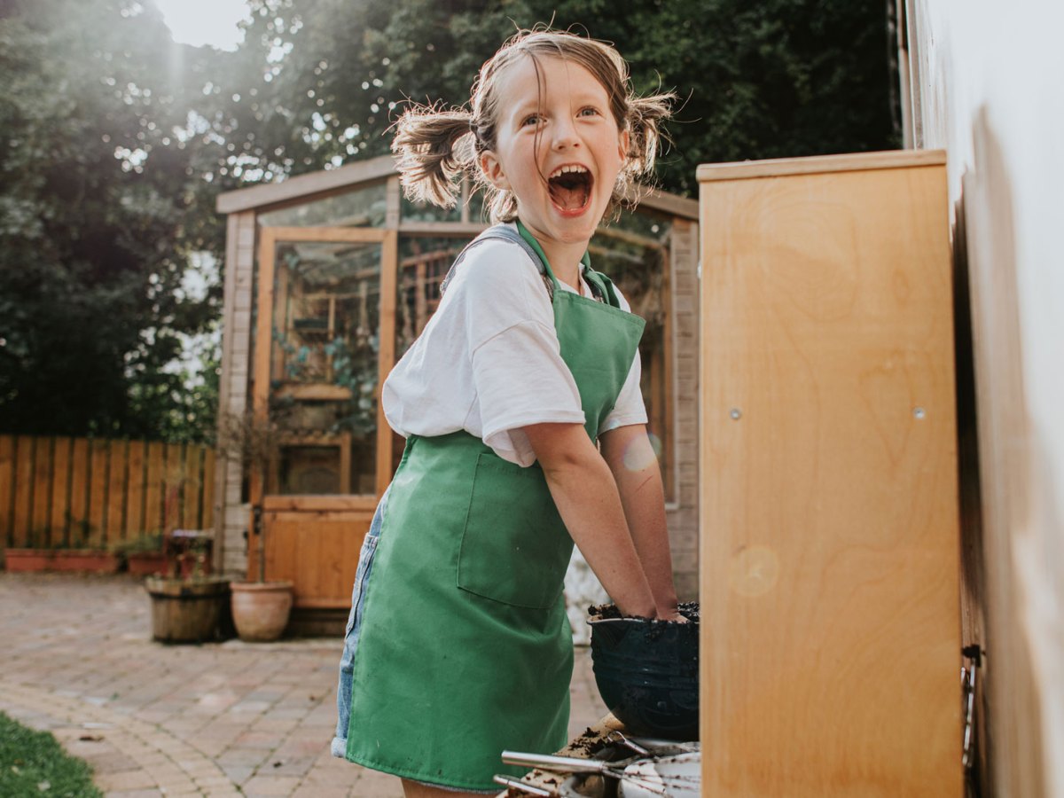 Aufgeregtes Mädchen spielt draußen in einer Matsch-Küche und stiftet Chaos.
