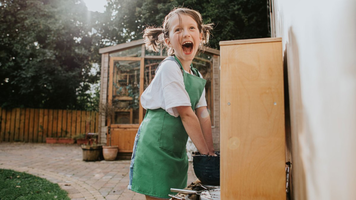 Aufgeregtes Mädchen spielt draußen in einer Matsch-Küche und stiftet Chaos.