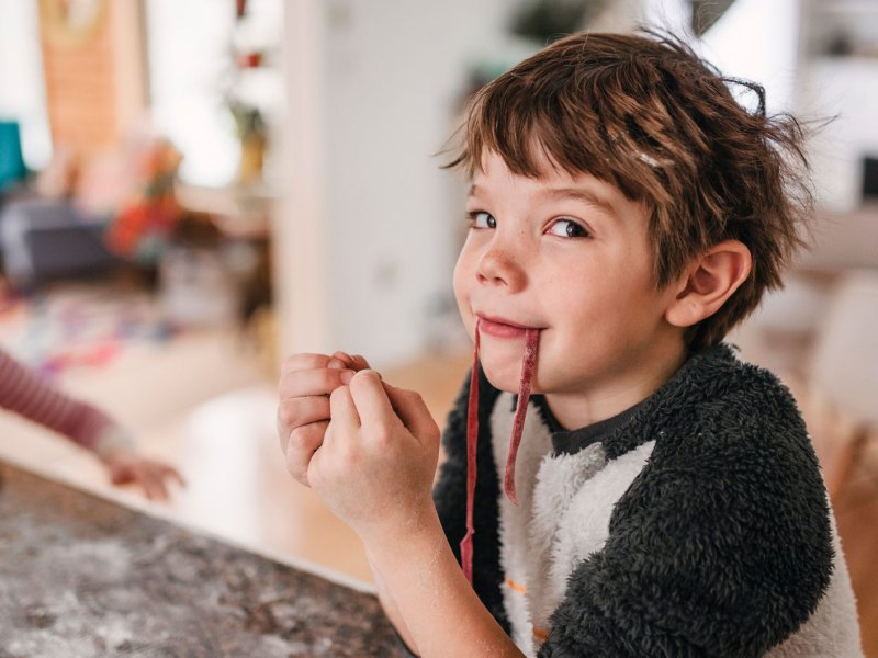 Porträt eines Jungen, der in der Küche sitzt und frische Pasta isst.