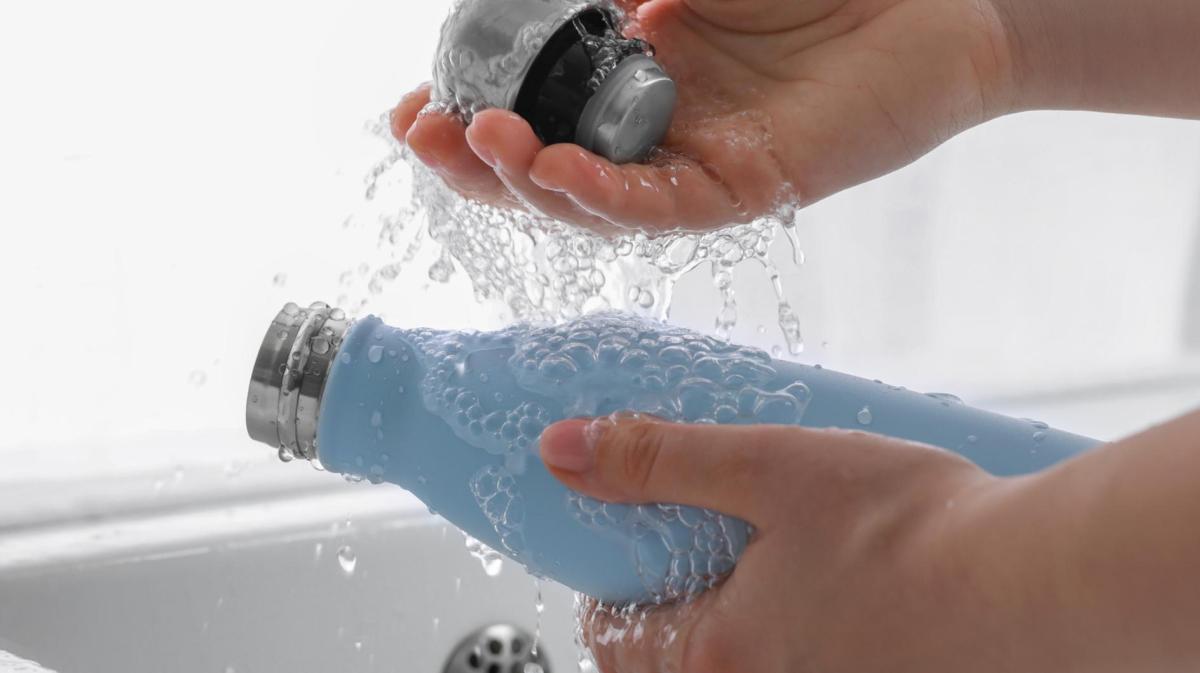 Frau spült eine Thermoskanne mit Wasser aus.