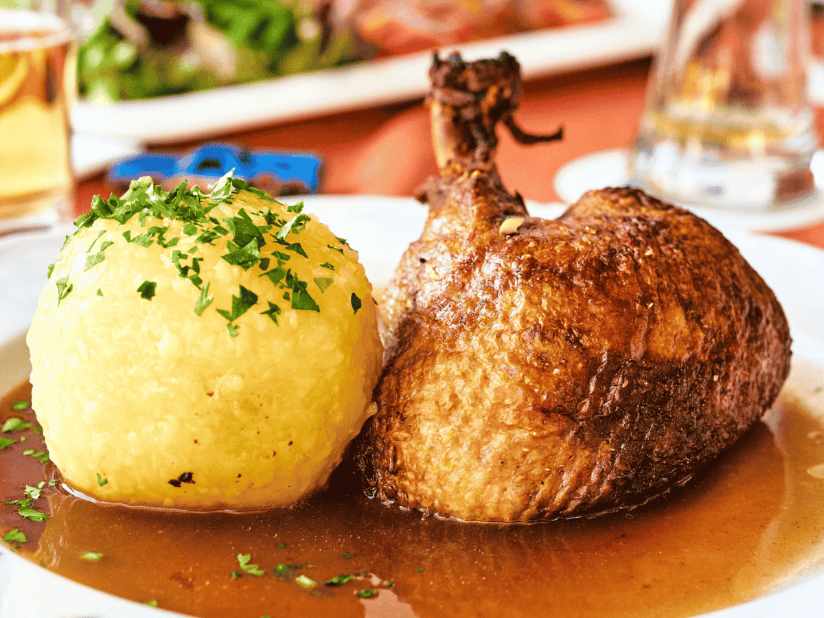 Gro&szlig;er Kartoffelklo&szlig; neben gebratener Entenkeule auf wei&szlig;em Teller.