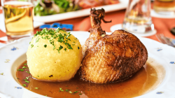 Großer Kartoffelkloß neben gebratener Entenkeule auf weißem Teller.