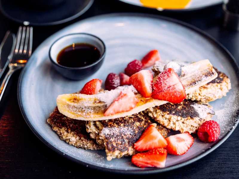 Perfektes Frühstück für Fans von veganen Desserts: Ein Teller mit fluffigen, goldbraunen veganen Pancakes, garniert mit frischen Beeren und Ahornsirup.