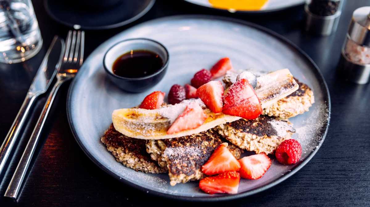 Perfektes Frühstück für Fans von veganen Desserts: Ein Teller mit fluffigen, goldbraunen veganen Pancakes, garniert mit frischen Beeren und Ahornsirup.