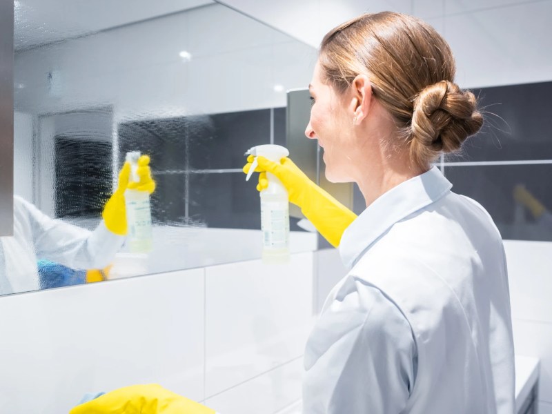 Eine blonde Frau sprüht einen Badezimmerspiegel ein