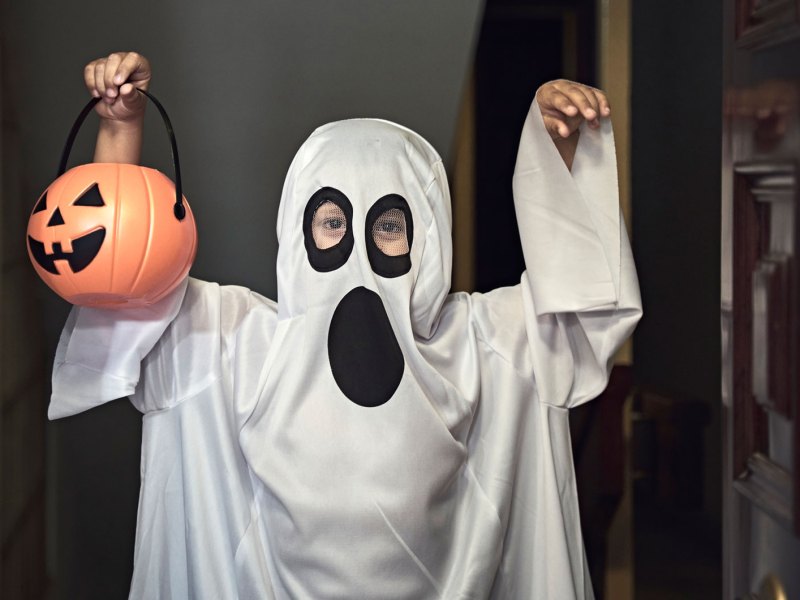 Kind als Geist verkleidet, mit einem kleinen Kürbis-Korb in der Hand.