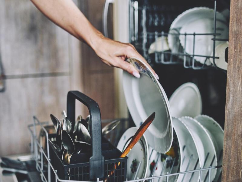 Person räumt Geschirr in die Spülmaschine ein.