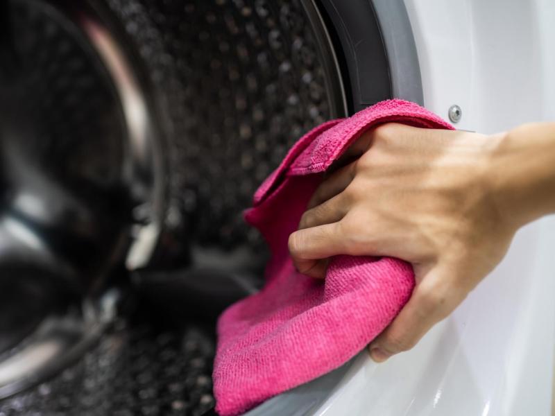 Frau macht die Dichtungen einer Waschmaschine mit einem pinken Tuch sauber.