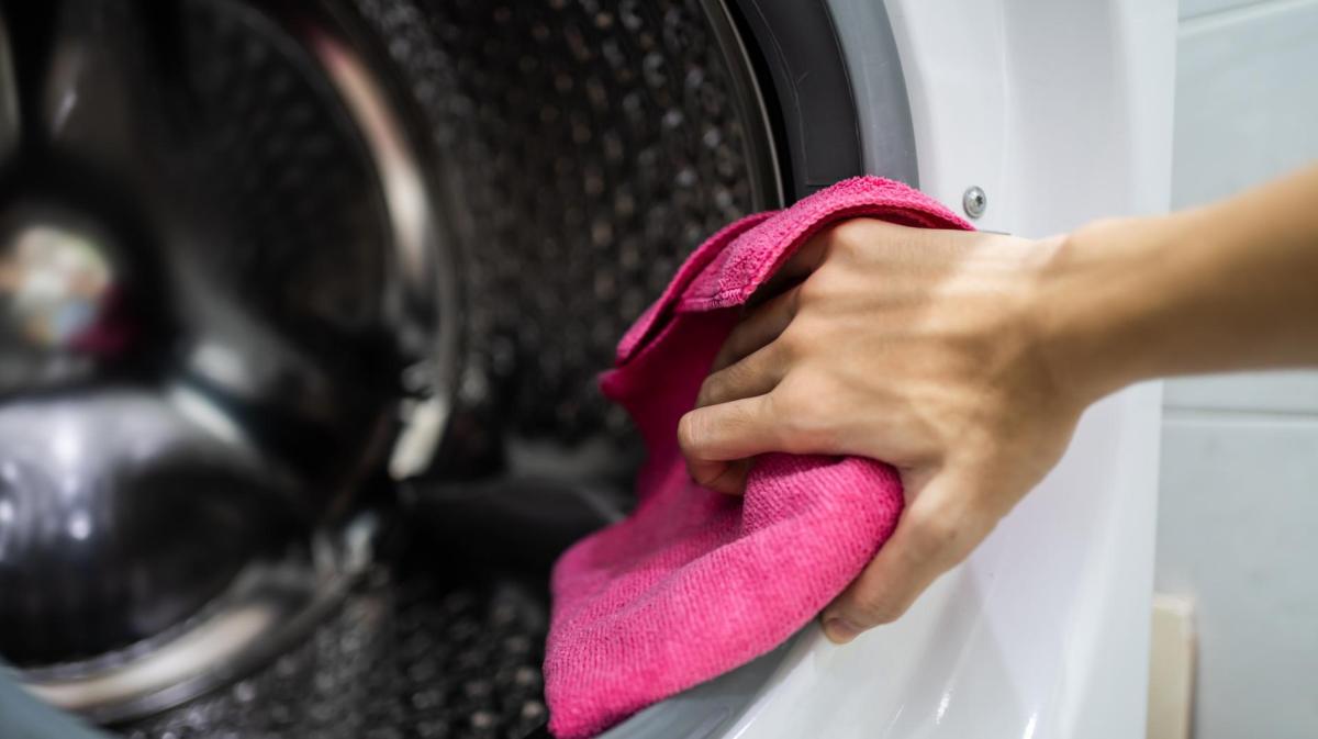 Frau macht die Dichtungen einer Waschmaschine mit einem pinken Tuch sauber.