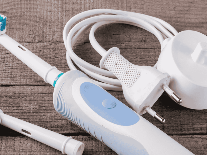 Elektrische Zahnbürste und Ladestation liegen auf Holztisch.