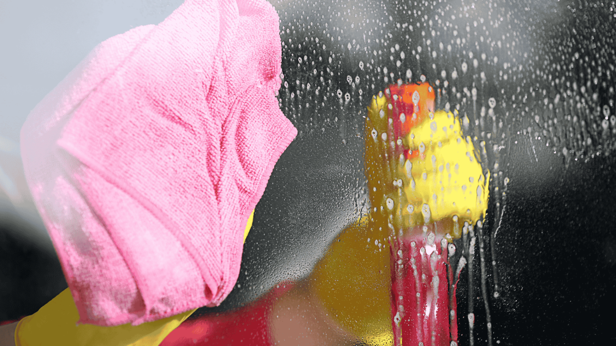 Person sprüht Fenster ein und wischt mit Tuch nach.