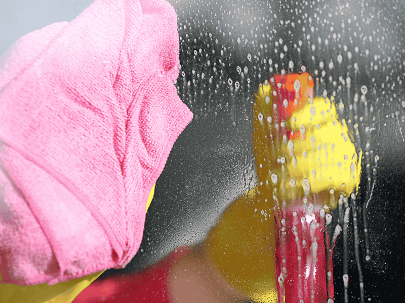 Person sprüht Fenster ein und wischt mit Tuch nach.