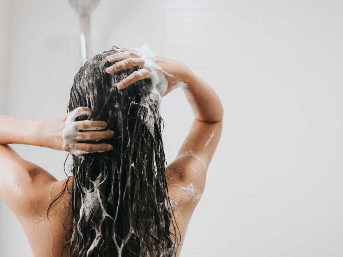 Frau beim Haare waschen unter der Dusche &ndash; Tipps f&uuml;r gl&auml;nzendes, gesundes Haar.