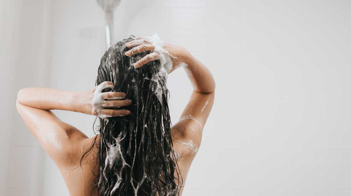 Frau beim Haare waschen unter der Dusche – Tipps für glänzendes, gesundes Haar.
