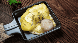 Raclette-Pfännchen mit Kartoffeln, Käse und Kräutern.