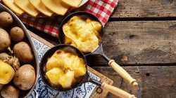 Raclette-Pfännchen mit Kartoffeln und Käse auf Holztisch.