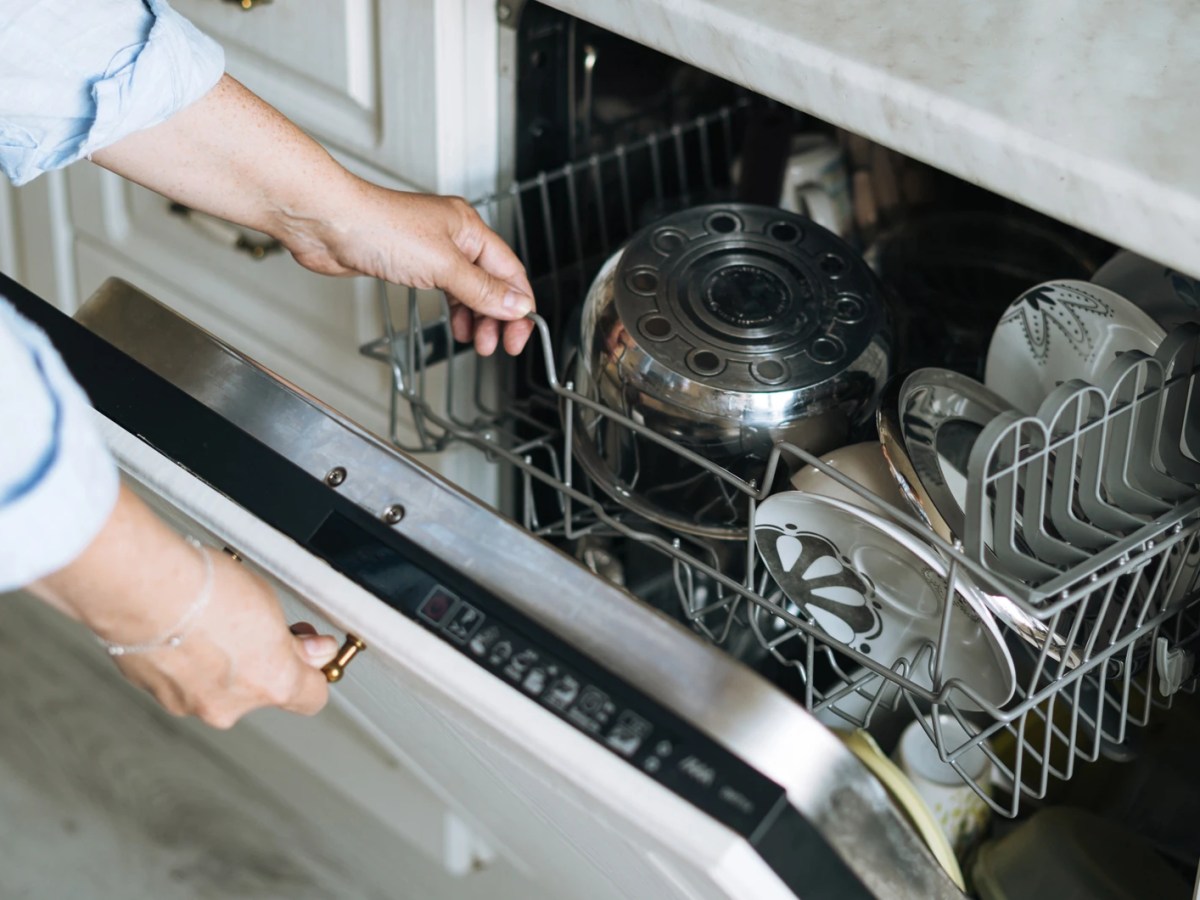 Frau öffnet fertige Spülmaschine