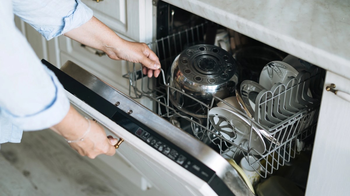 Frau öffnet fertige Spülmaschine