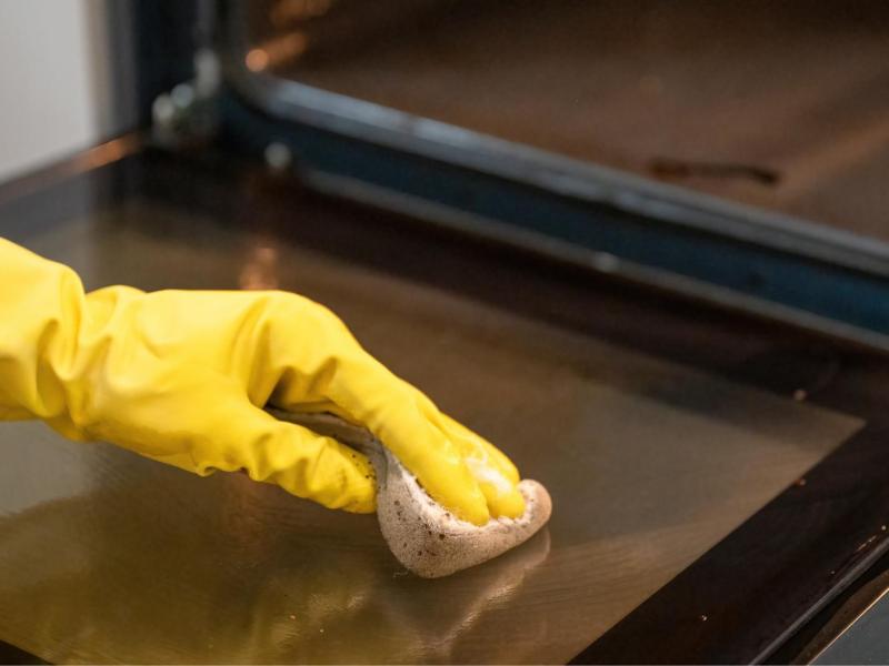 Frau reinigt die Scheibe des Backofens.