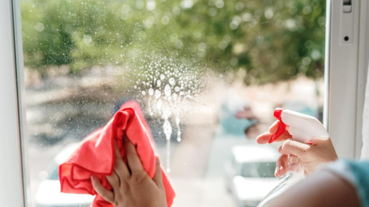 Frau putzt ihre Fenster mit einem Tuch und einem Reiniger.