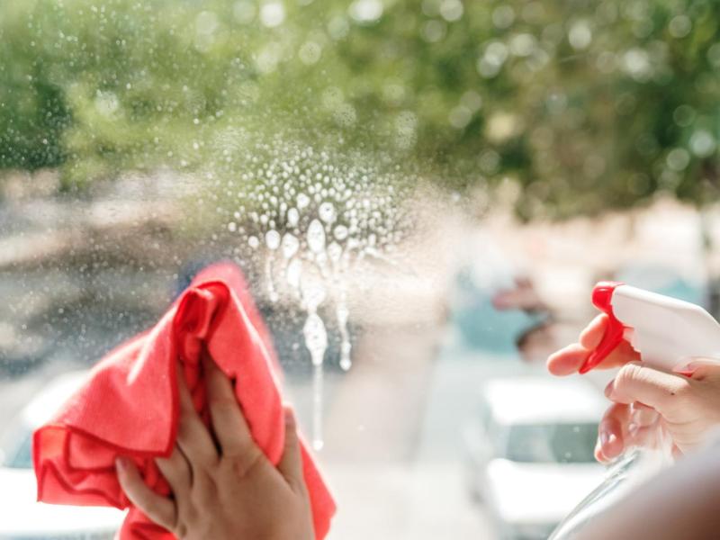 Frau putzt ihre Fenster mit einem Tuch und einem Reiniger.