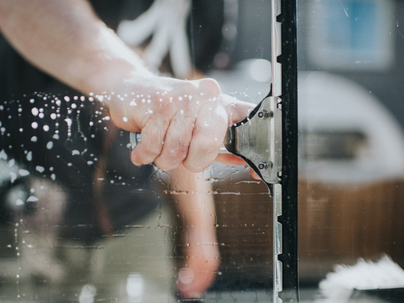 Mann reinigt seine Fenster mit einem Abzieher.
