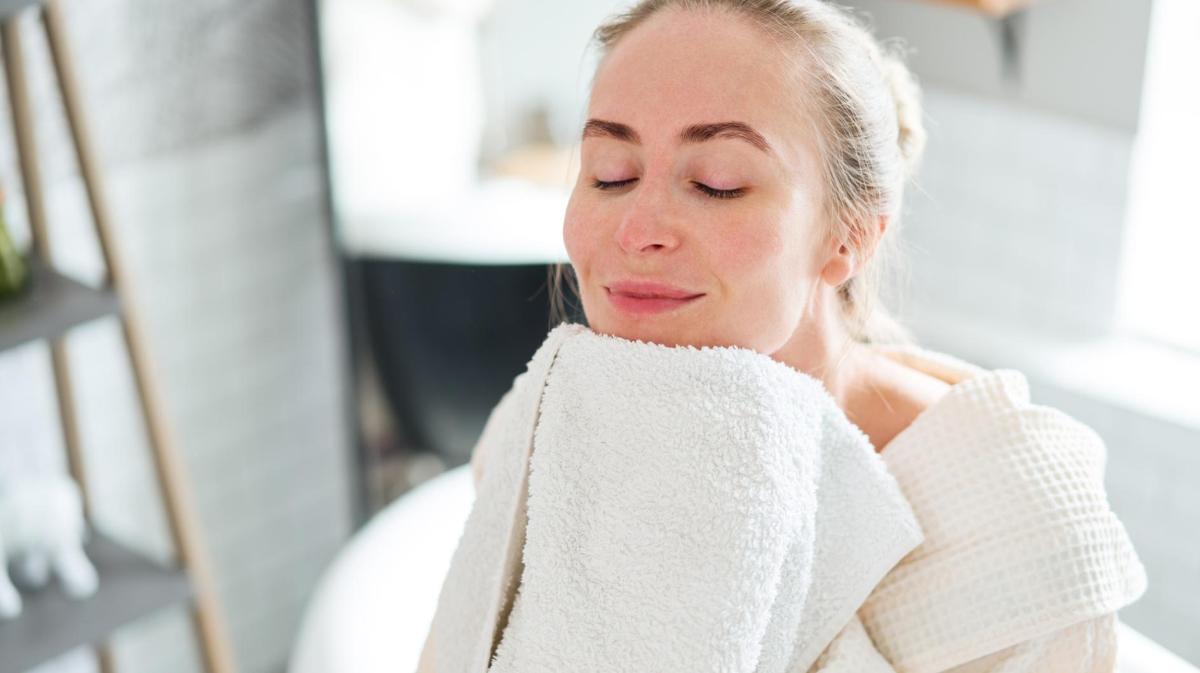 Frau reibt ihr Gesicht an ein Handtuch.