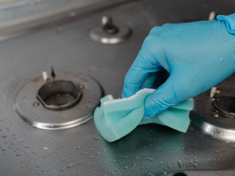 Person reinigt einen Herd mit einem Schwamm.