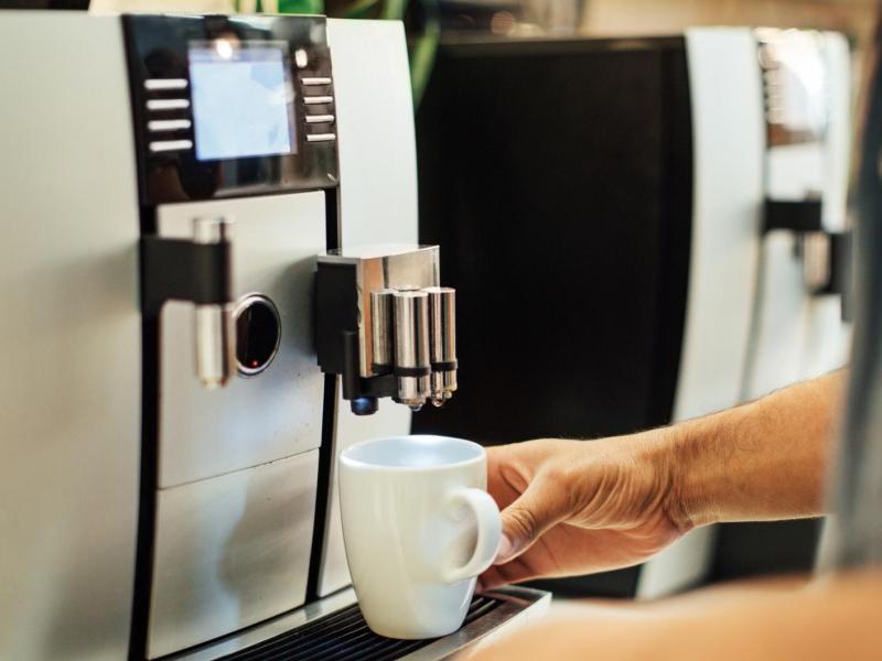 Mann stellt eine Tasse in einen Kaffeevollautomat .