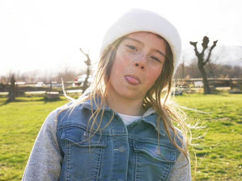 Mädchen an einem schönen Herbsttag draußen, streckt frech die Zunge raus.