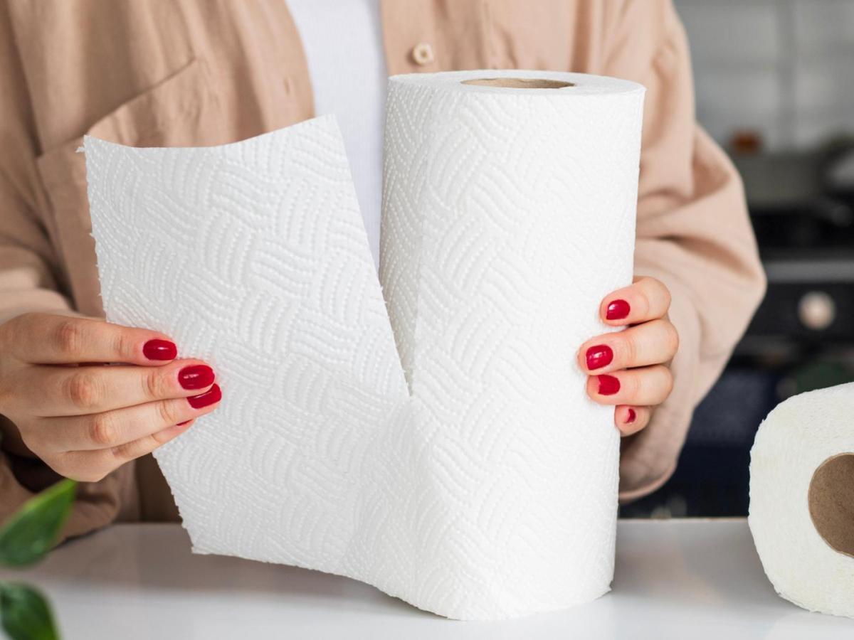 Frau mit roten N&auml;geln rei&szlig;t ein St&uuml;ck K&uuml;chenkrepp ab.