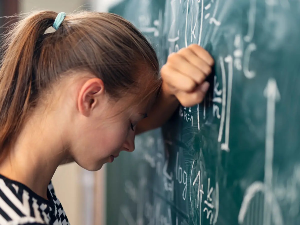 M&auml;dchen lehnt mit Kopf an Tafel, auf der eine Matheaufgabe steht.
