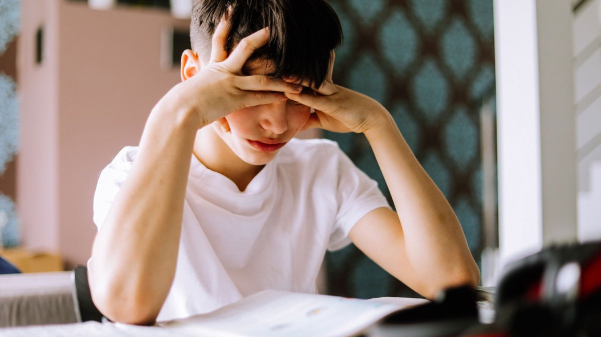 Junge, ca. 12 Jahre, schaut verzweifelt auf seine Hausaufgaben.