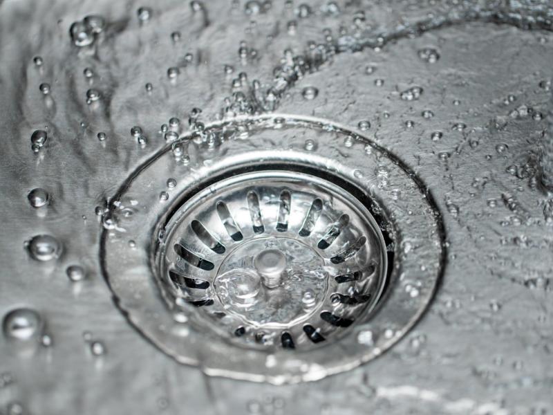 Wasser fließt in den Abfluss eines Edelstahlspülbeckens.