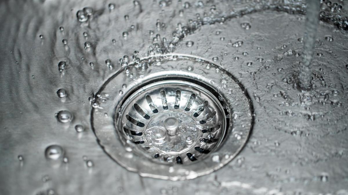 Wasser fließt in den Abfluss eines Edelstahlspülbeckens.