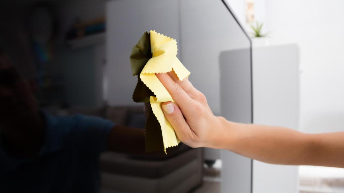 Frau wischt mit einem Mikrofasertuch über den Fernsehbildschirm.