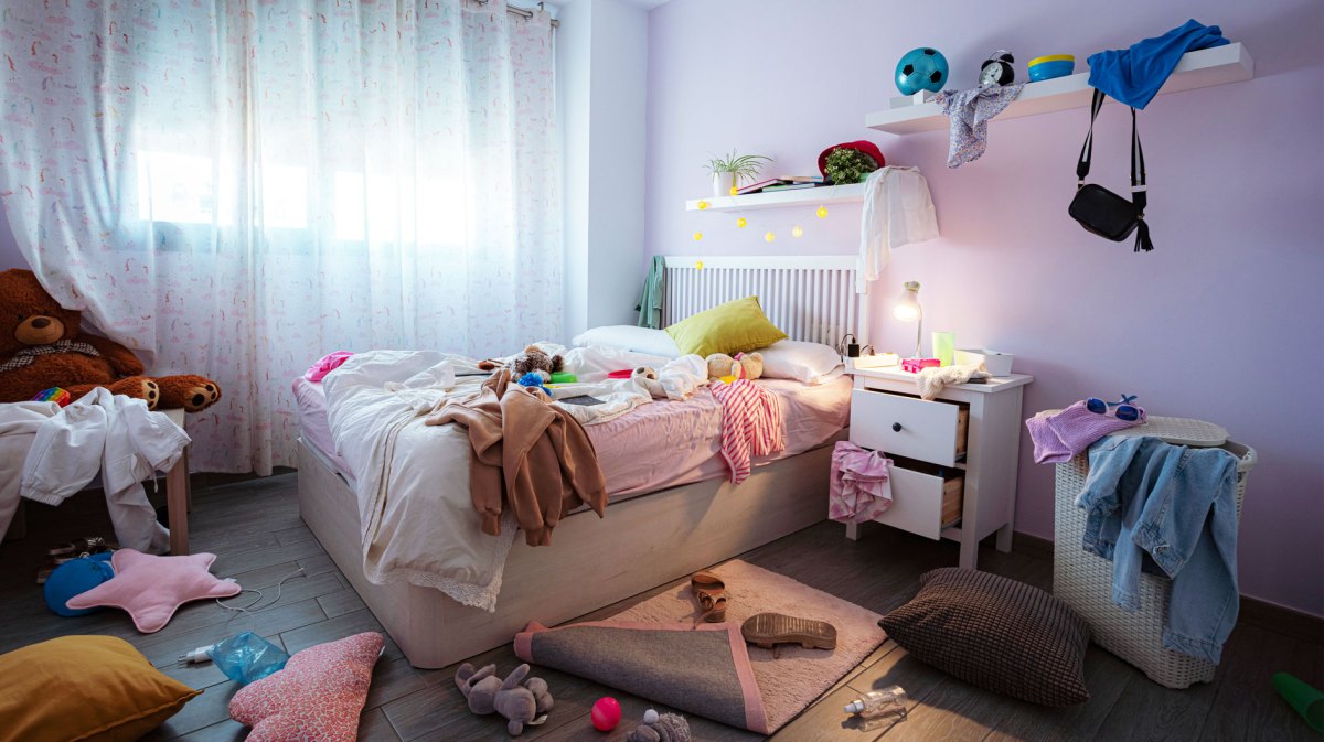 Unordentlichen Jugendzimmer: Klamotten überall verteilt, Teppich halb aufgerollt, Wäschekorb quillt über.
