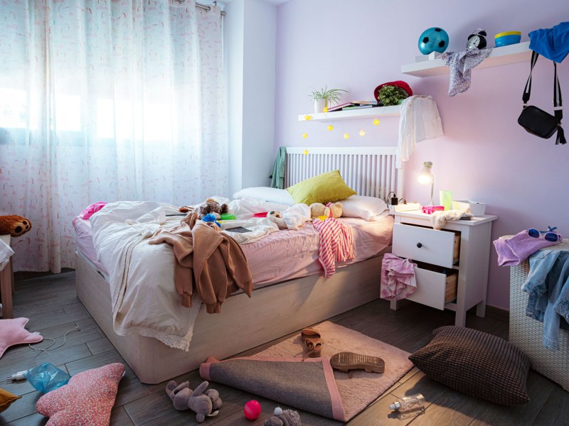 Unordentlichen Jugendzimmer: Klamotten überall verteilt, Teppich halb aufgerollt, Wäschekorb quillt über.