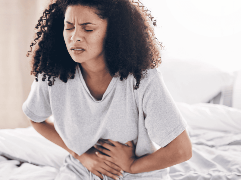 Bauchschmerzen, schwarze Frau im Bett mit Bauchkrämpfen, Magenschmerzen. Gesundheit, medizinischer Notfall Frau mit Verdauungsproblemen im Schlafzimmer.
