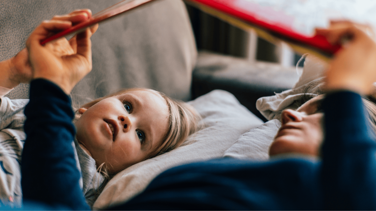 Mutter und Tochter liegen auf der Couch und lesen ein Buch.
